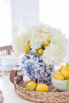 a blue and white vase filled with flowers next to lemons on a wicker tray