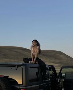 a woman sitting on the back of a black jeep in front of a desert landscape