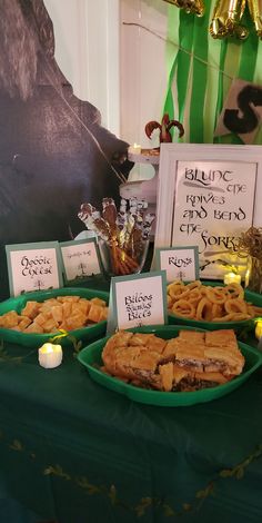 a table topped with plates filled with food next to candles and signs on green cloth