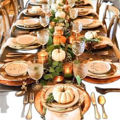 a table set for thanksgiving dinner with pumpkins and greenery on the place settings