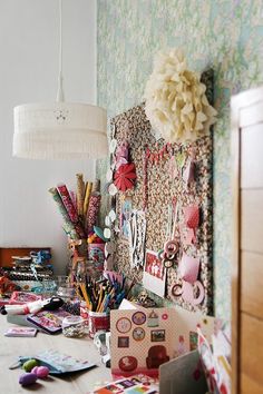 a cluttered desk with lots of crafting supplies on it and a lamp hanging from the ceiling