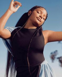 a woman with braids and a black top is holding her arms up in the air