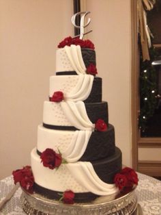 a three tiered wedding cake with red roses on the bottom and black, white, and grey layers