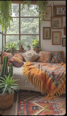 a room with plants and pictures on the wall, including a bed in front of a window