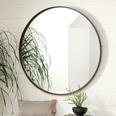 a round mirror hanging on the wall next to a table with a pillow and potted plant