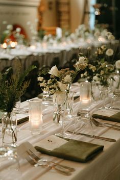 the table is set with silverware and white flowers in vases on each side