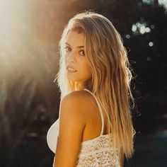 a beautiful young blonde woman standing in front of the sun wearing a white tank top