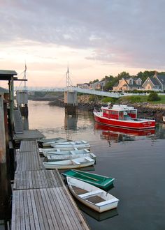 several small boats are docked in the water near a dock with houses and a bridge