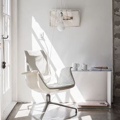 a white chair sitting in the middle of a room next to a wall mounted light fixture