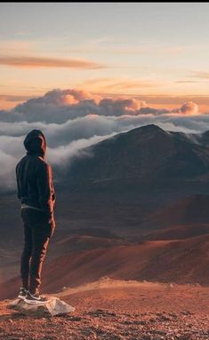 a man standing on top of a mountain looking out at the clouds in the distance