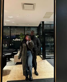 a man and woman taking a selfie in front of a hotel lobby door with their cell phone