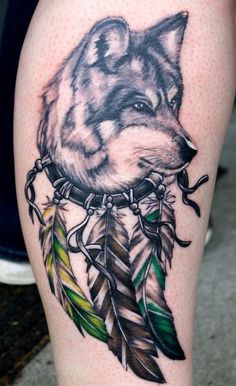 a tattoo with an image of a wolf and feathers on the leg, which is also in color