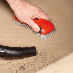 a hand with a brush on top of sand next to a black shoe and a red object