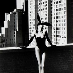 a woman in a bathing suit and hat standing on a wall with buildings behind her