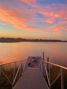 two people laying on a dock at sunset