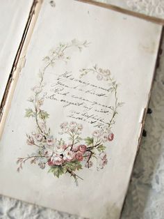 an old book with flowers on it sitting on a lace tablecloth covered bed sheet