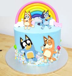 a cake with cartoon characters on it sitting on top of a wooden table next to a rainbow