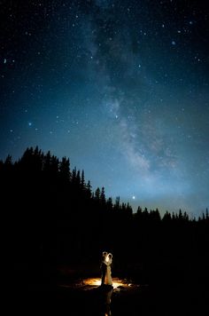 a man and woman standing in the middle of a field under a night sky filled with stars