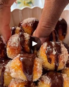 a person touching chocolate covered doughnuts in a bowl