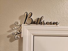 a bathroom sign hanging on the wall above a white door with an ornately decorated frame