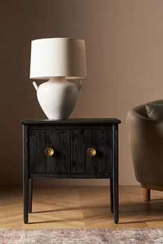 a white vase sitting on top of a wooden table next to a chair and lamp