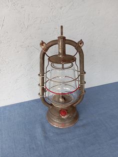 an old fashioned lamp is sitting on a blue tablecloth with white wall in the background