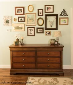 there is a dresser in the room with many framed pictures on the wall above it