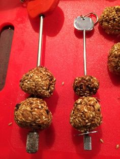 four birdseed balls on a red tray with a measuring spoon next to one that has three holes in the middle