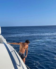 a shirtless man standing on the bow of a boat in the open water,