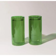 two green glass tumblers sitting next to each other on a white surface with shadows