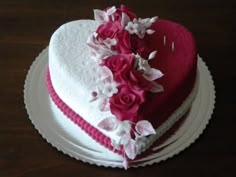 a heart shaped cake with pink and white flowers on the top is sitting on a plate