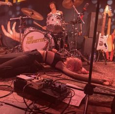 a man laying on the ground in front of a drum kit and another person with their legs up