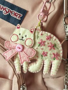 a pink and white cat keychain hanging from a purse with a tag attached to it