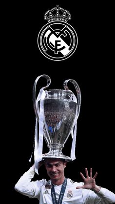 a man holding up a silver trophy in front of his face with the real madrid logo above it