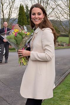 a woman holding flowers in her hand while standing on the sidewalk with other people behind her