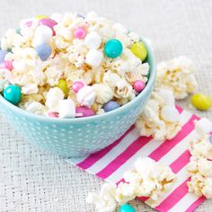 a blue bowl filled with white and pink candy popcorn on top of a striped napkin