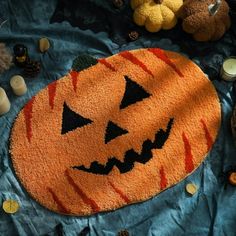 a halloween pumpkin rug on a bed with candles and teddy bears in the back ground