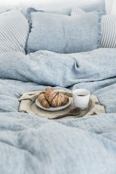 a plate with croissants on it sitting on a bed next to a cup and saucer