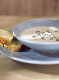 a bowl of soup on a blue plate with two pieces of bread next to it