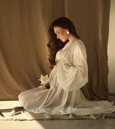 a pregnant woman sitting on the floor holding a flower