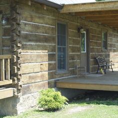 a porch with a bench on it next to a log cabin style building and green grass