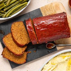 sliced meatloaf on cutting board next to bowl of green beans and other foods