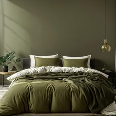 a bed with green comforter and pillows in a room next to a plant on the wall