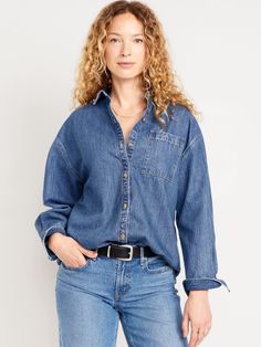 a woman wearing a denim shirt and jeans with her hands in her pockets, posing for the camera