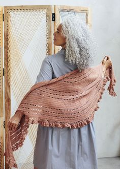 an older woman wearing a shawl standing in front of a weaving machine and looking off into the distance