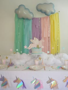 a table topped with cake and cupcakes covered in frosting next to rainbow streamers