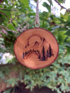 a wooden ornament hanging from a tree with trees and mountains in the background