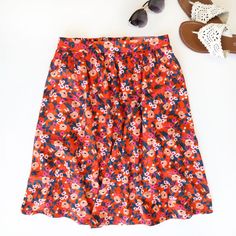 a pair of sandals, sunglasses and an orange flowered skirt on a white surface