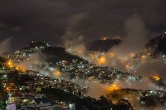 the city lights shine brightly in the foggy night sky as it sits on top of a hill