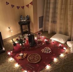 a table topped with pizza and other food on top of a red cloth covered floor